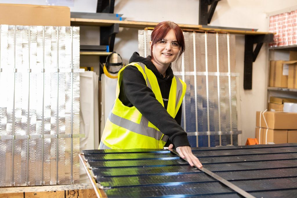 A young woman in high vis and safety goggles measure a solar thermal panel with a large metal roller as a Scottish Apprenticeship Awards Finalist 2026