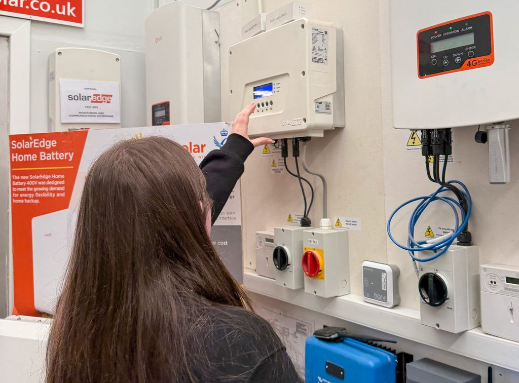 A young woman on work experience at aes renewables examines a solar inverter in a technology showroom at aes renewables